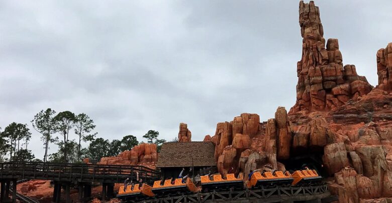 The Big Thunder Mountain Railroad coaster speeds along red rock tracks beneath swirling clouds at Magic Kingdom.