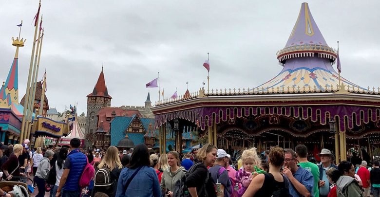 Visitors enjoy the lively atmosphere by the vibrant carousel at the amusement park, with clouds overhead setting the scene.