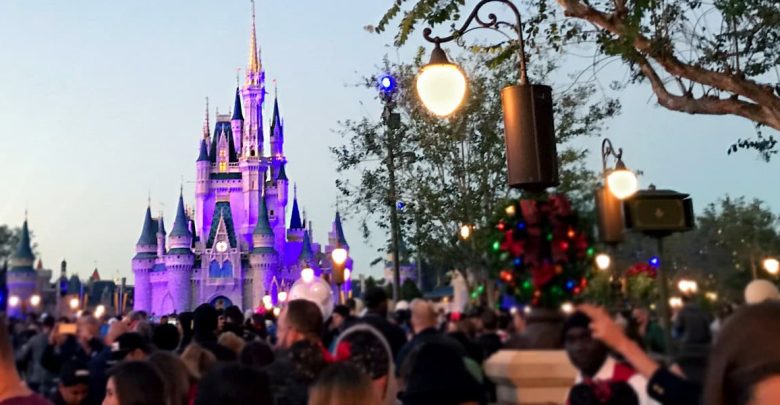 Evening crowds gather before Cinderella Castle at Magic Kingdom, glowing with lights amid trees and streetlamps.