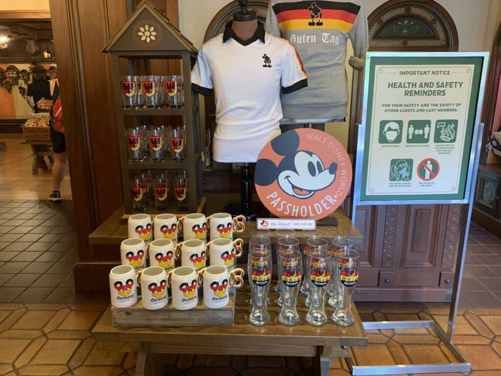 Mickey Mouse mugs, glasses, shirts, and the Annual Passholder Program sign on display at a Disney World merchandise shop.