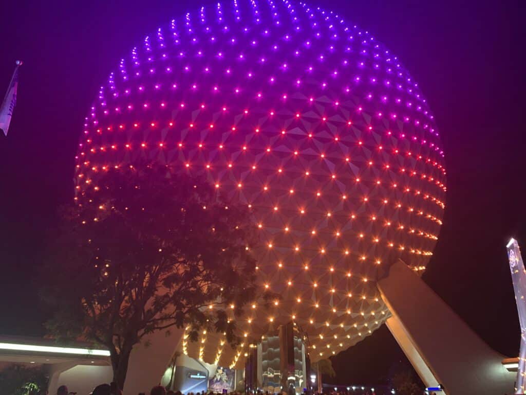 Spaceship Earth glowing in vibrant purple and orange at EPCOT, with guests gathered below during The Four Park Challenge at Disney World.