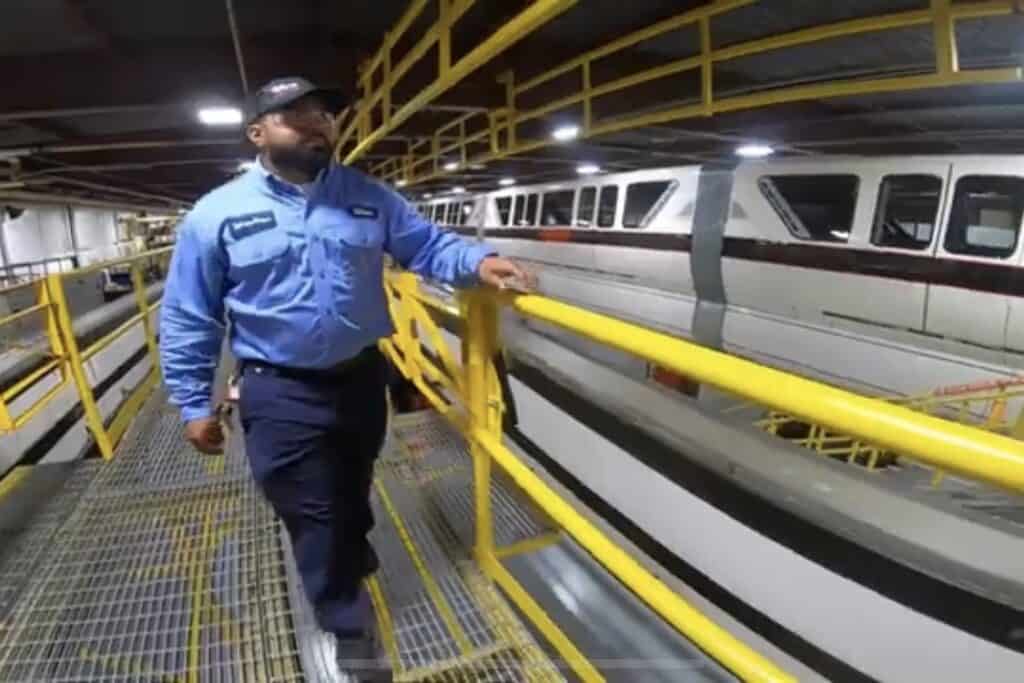 A team member in blue uniform walks beside a sleek train indoors, prepping for job fairs inspired by Disney’s legendary efficiency.