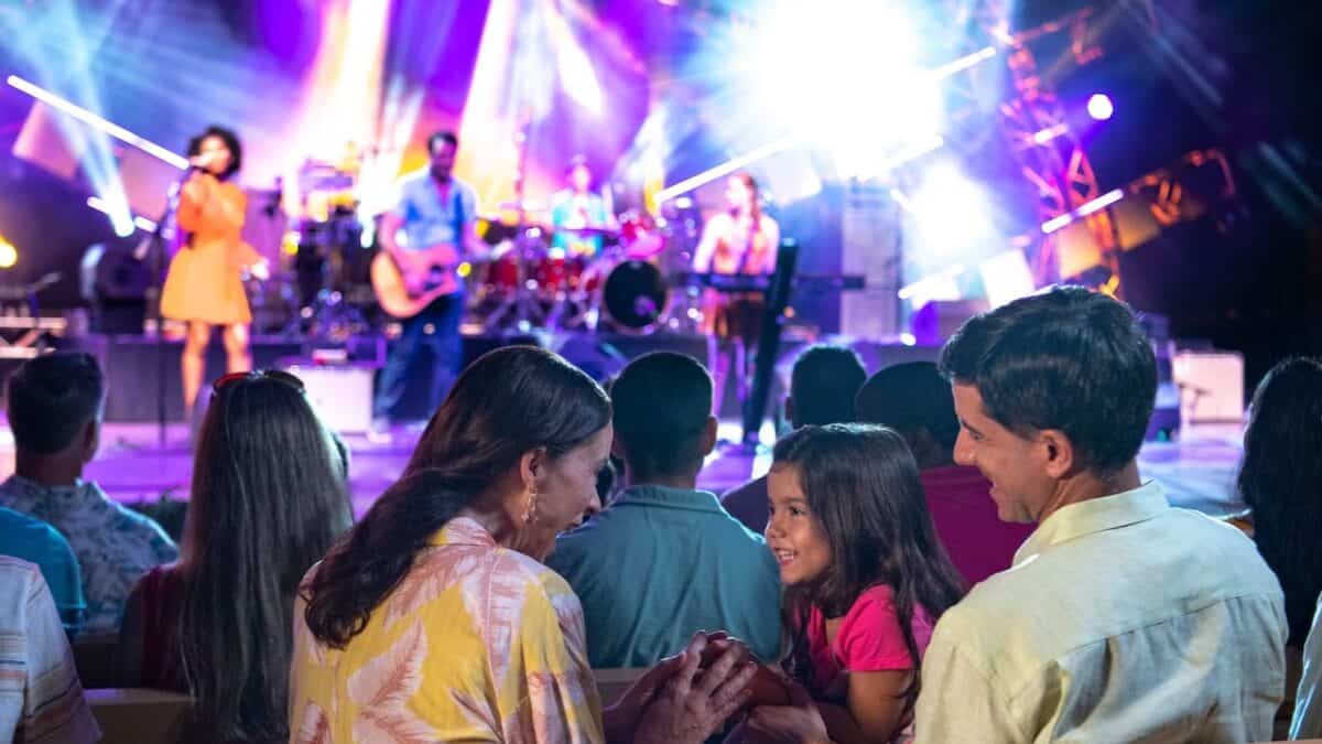 Guests at EPCOT smile and enjoy Garden Rocks as the band energizes the crowd on a vibrant, illuminated America Gardens Theatre stage.