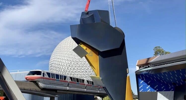 A crane lifts a towering metal structure beside the Epcot monorail and Spaceship Earth during exciting park construction.