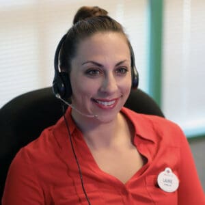 Friendly Disney Cast Member with headset and name badge smiling at her office desk, ready to answer questions about upcoming job fairs.