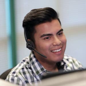 Cast member in a plaid shirt and headset at a Disney World office desk, ready to help guests with upcoming job fair details.