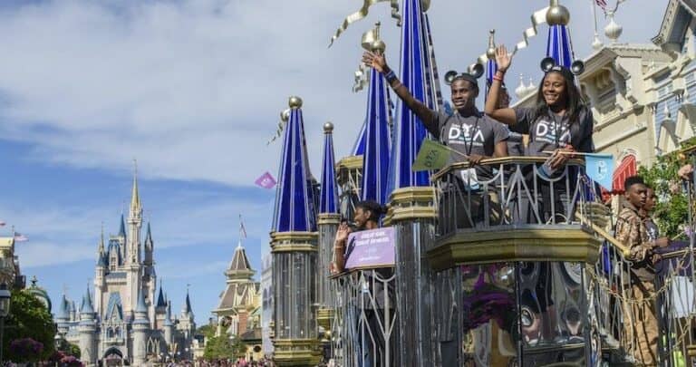Colorful parade float passes in front of Cinderella Castle at Disney World, as performers wave to cheering guests along Main Street.