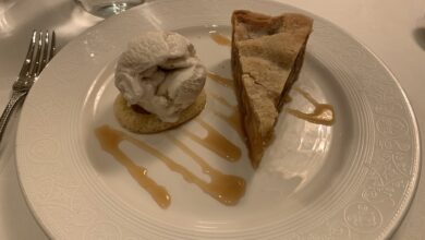 Decadent pie and creamy ice cream atop cake, drizzled with caramel, served on a white plate at a theme park dessert café.