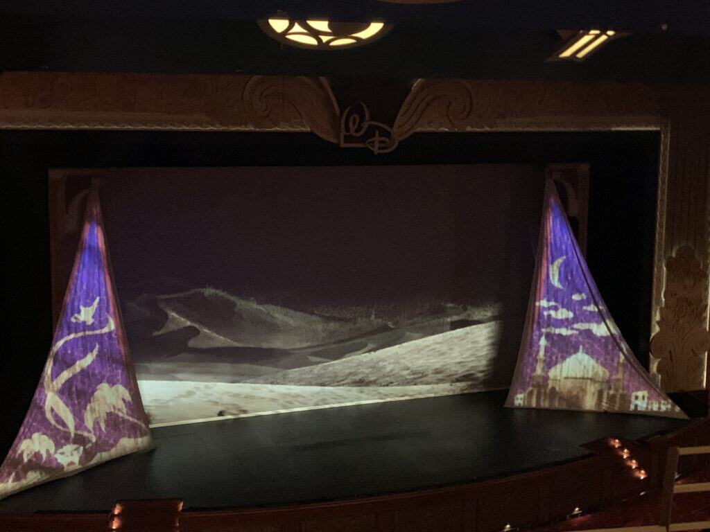 The Disney Fantasy stage glows with purple lights and a black-and-white desert scene, casting a magical theatrical atmosphere.