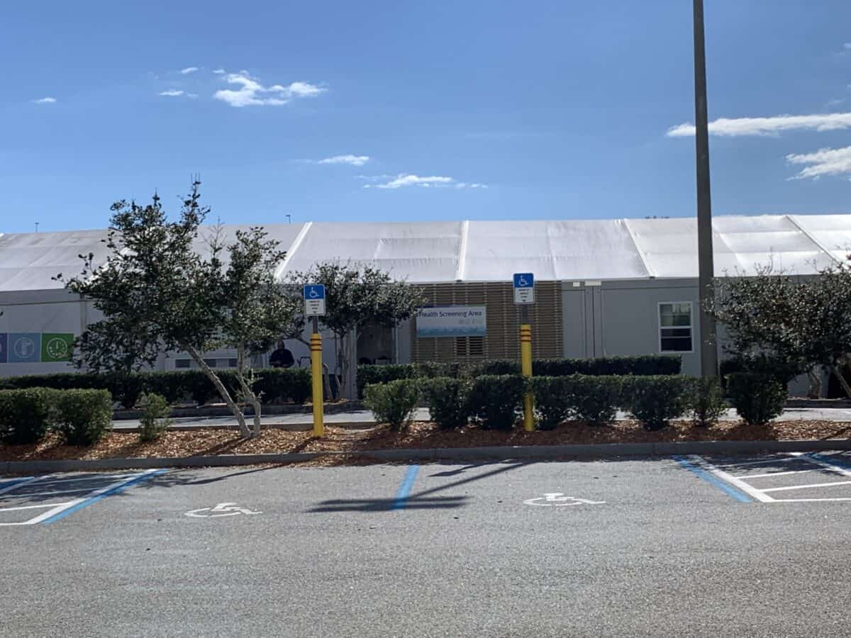 Accessible parking spots in front of a white building, with trees and bushes, like the organized lots by the Disney Fantasy terminal.