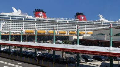 The Disney Cruise Line ship awaits guests at port, with parked cars beneath a red-roofed terminal in the foreground.