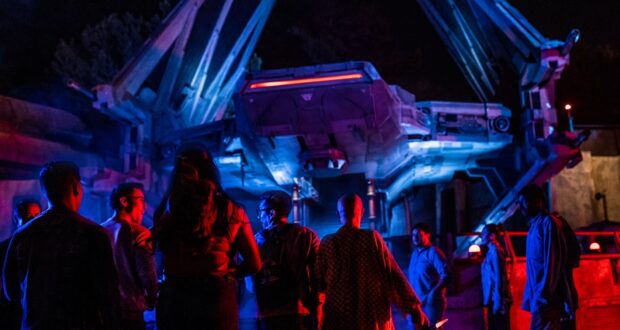 Guests gather beneath vibrant lights beside a massive, futuristic spaceship at Disney's Star Wars: Galaxy's Edge at night.