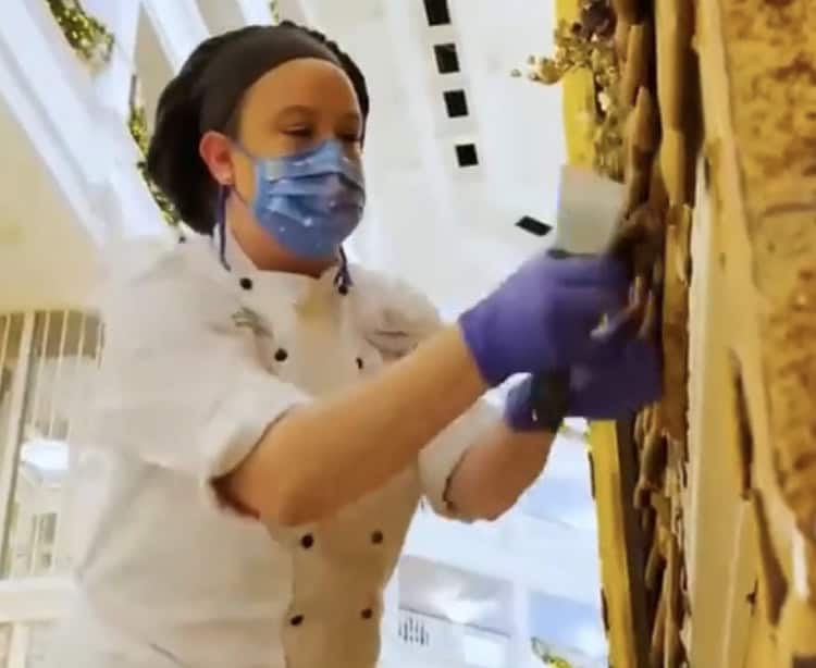 A chef at a themed attraction decorates a giant wall with chocolate, making it look like a festive Gingerbread House.