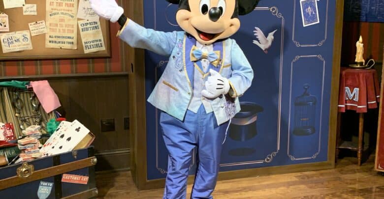 Mickey Mouse greets guests in a blue suit inside a magical Disney World room, surrounded by themed props and ticket offer signs.