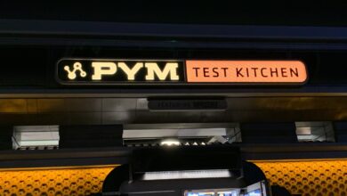 PYM TEST KITCHEN sign glows in yellow and orange above the Avengers Campus entrance at night, inviting guests inside.