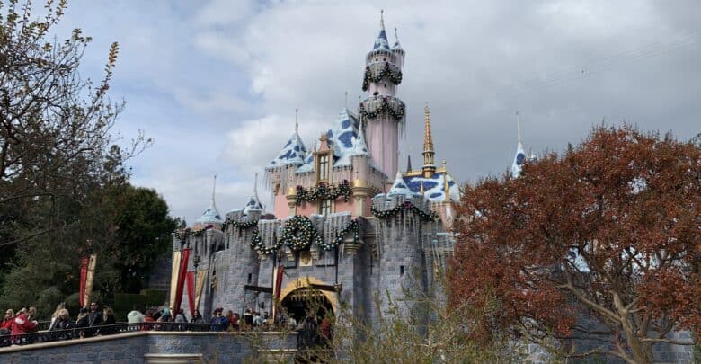 Sleeping Beauty Castle decked out for the holidays at Disneyland, with festive crowds on the bridge under overcast skies.