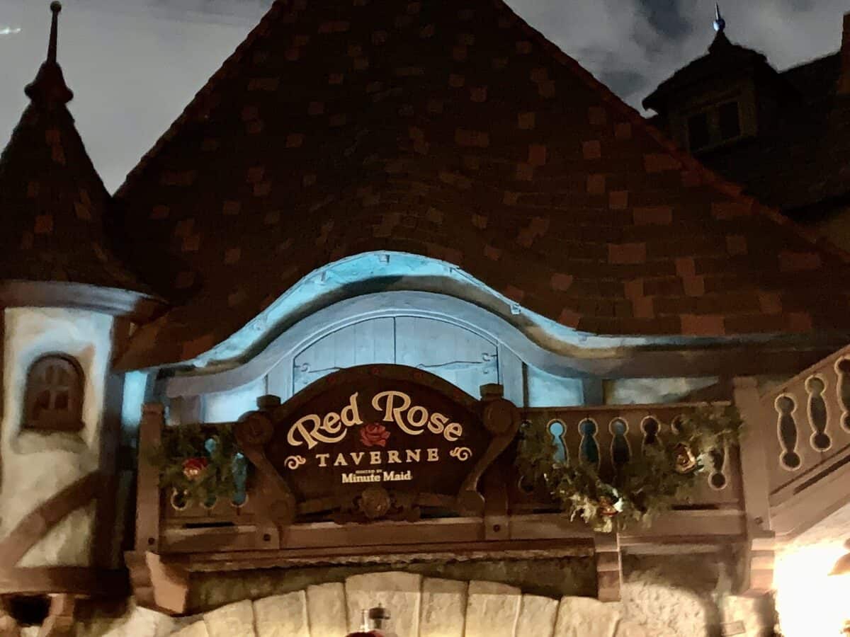 The Red Rose Taverne sign glows above its charming Fantasyland cottage at Disneyland, inviting guests to order delicious bites.