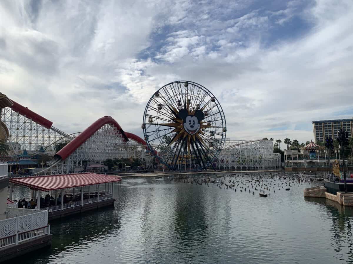 Mickey’s iconic Ferris wheel spins by the water at Disney California Adventure, inviting Park Pass guests under scenic clouds.