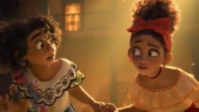 Mirabel and Isabela hold hands, looking worried inside Casita’s cozy living room, about to reveal Bruno’s secret at Encanto.