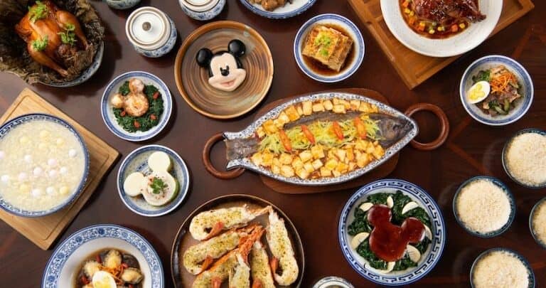 A festive table at a Disney park, featuring Chinese cuisine, rice bowls, tea cups, and a Mickey Mouse-shaped dessert specialty.