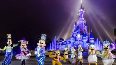 Beloved Disney characters gather in front of Cinderella Castle, aglow with dazzling purple and blue lights during a magical night.