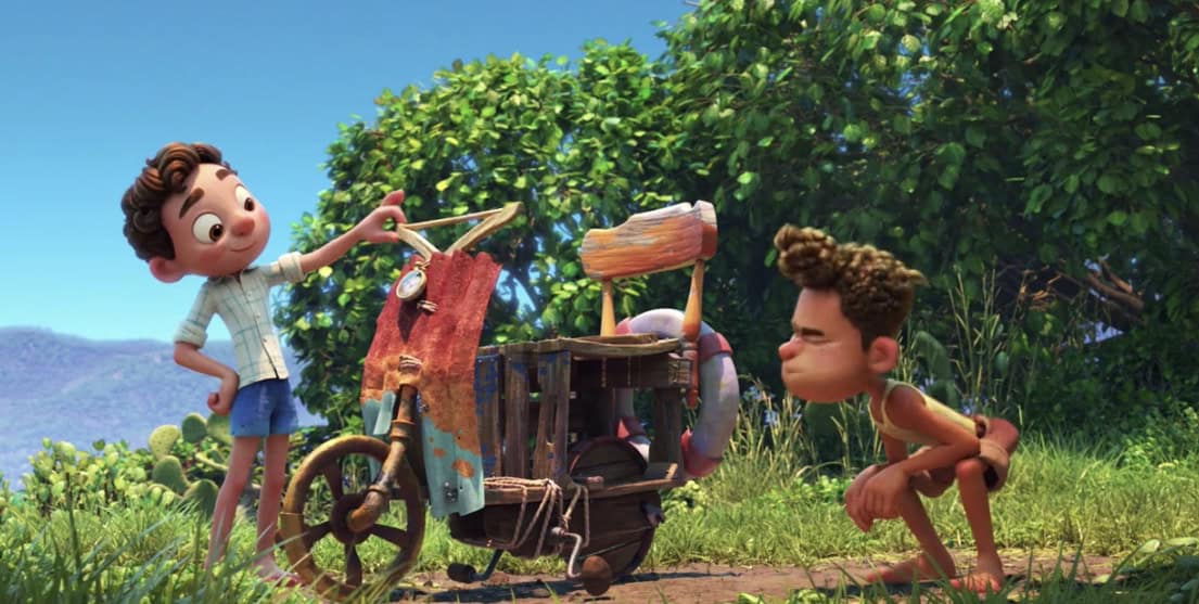 Luca and Alberto stand by their handmade bike in a sunlit meadow, trees behind them, chanting “Silenzio Bruno!” before adventure.
