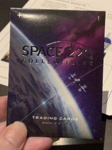 A guest displays a Space 220 Trading Cards pack showcasing the restaurant’s signature space station and planet artwork.