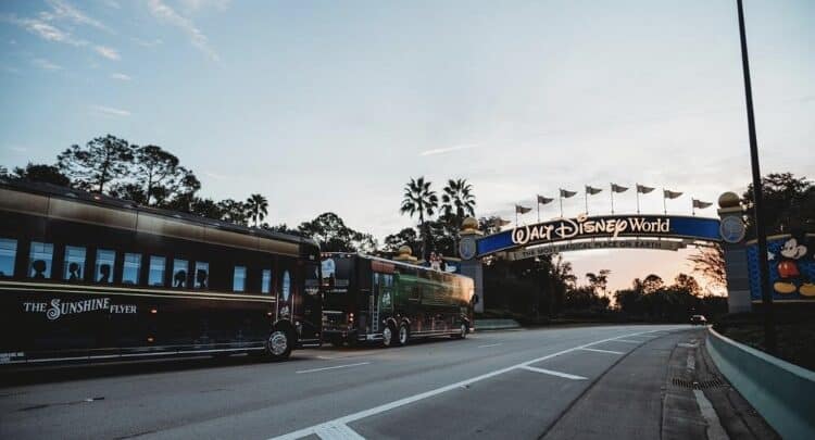 A Disney bus cruises beneath the iconic Walt Disney World entrance arch at sunset, framed by palm trees in true magical style.