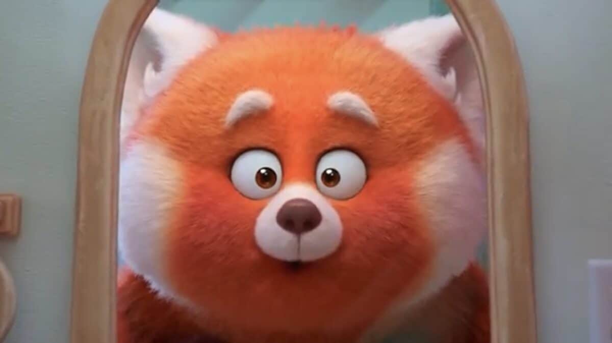 Turning Red’s adorable red panda character gazes wide-eyed at its reflection, evoking movie magic in a Disney Parks setting.