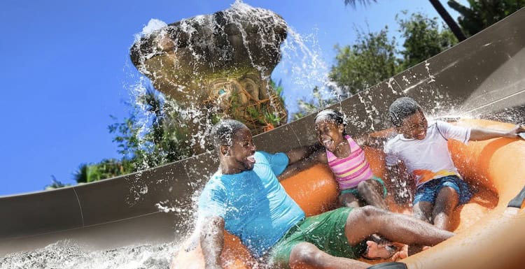 Guests enjoy a thrilling ride down a water slide on an orange raft, laughing together as they’re drenched by splashing waves.