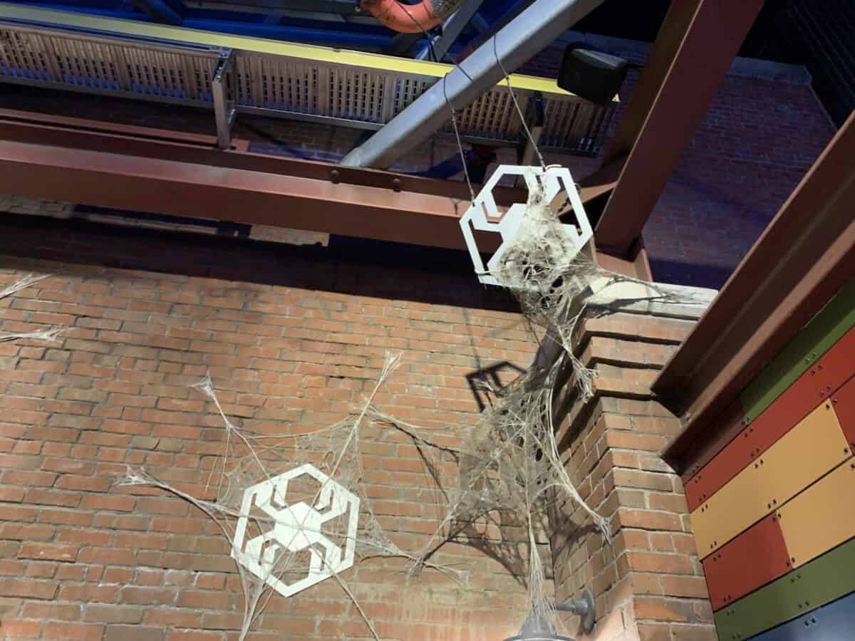 White hexagons and spooky spider webs decorate a brick wall under exposed beams, channeling Disneyland’s immersive atmosphere.