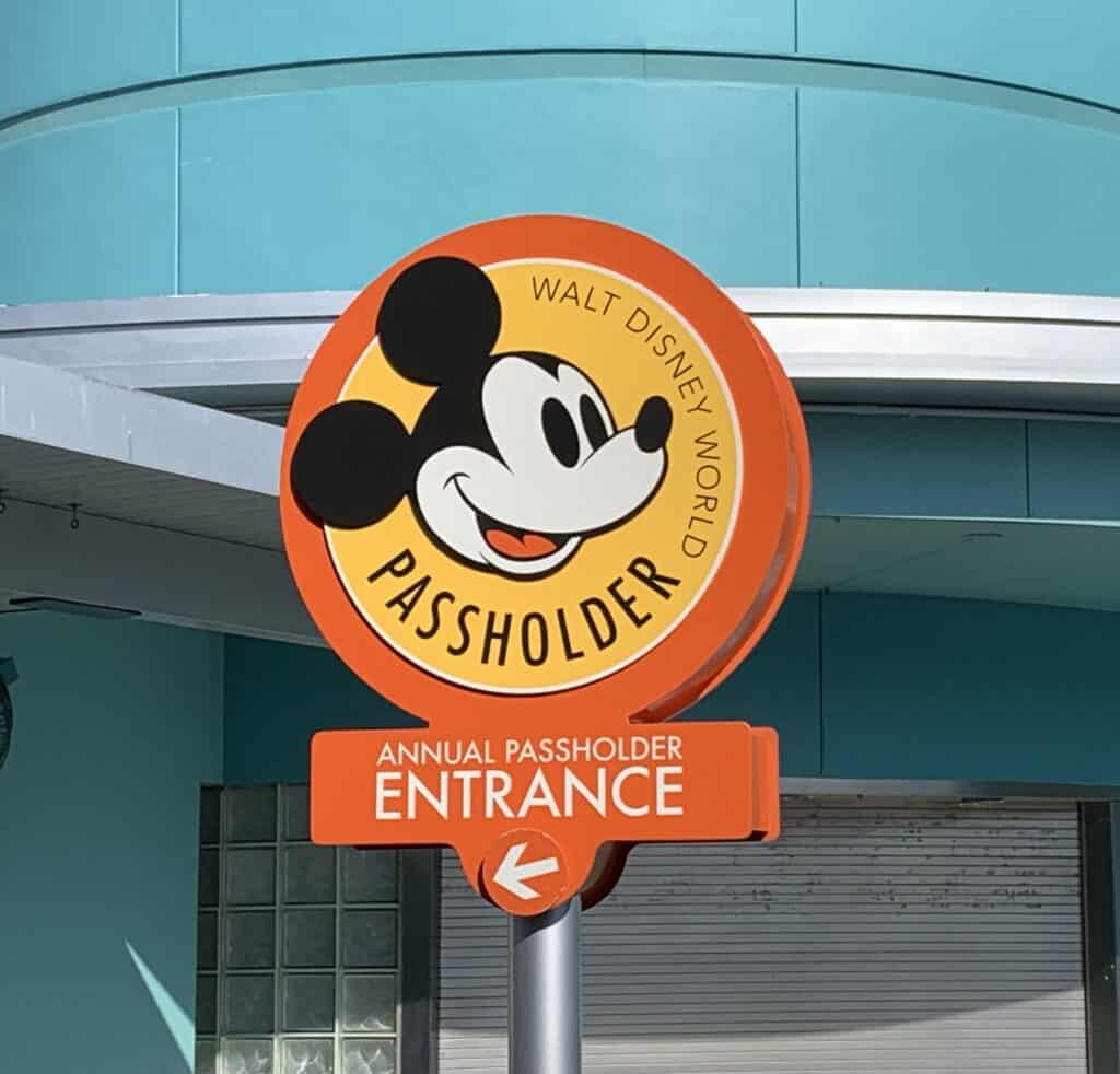 Bright orange sign at Disney World with Mickey Mouse, directing Annual Passholders left to their exclusive entrance.