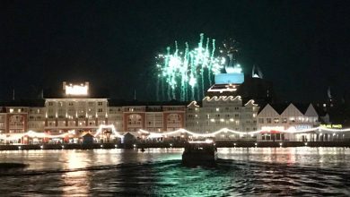 Green fireworks burst above waterfront buildings, reflecting on the water—just like Disney Enchantment outside Magic Kingdom.