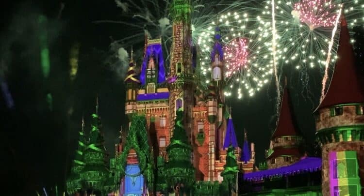 Cinderella Castle illuminated with vibrant lights as fireworks burst over Magic Kingdom at night.