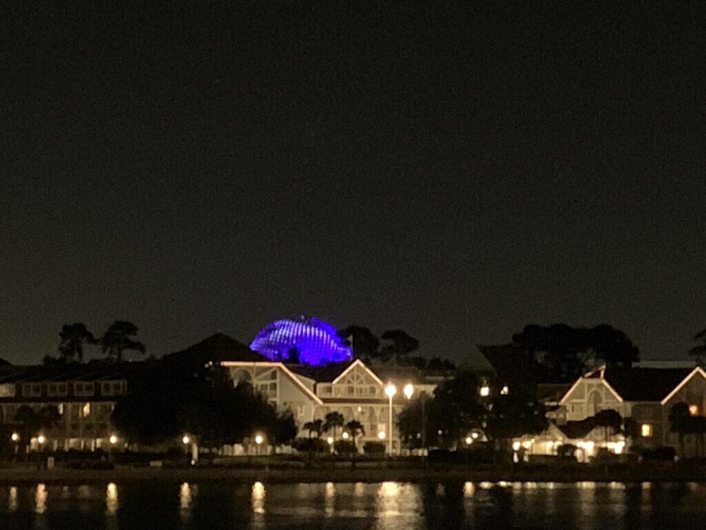 EPCOT at night with World Showcase buildings by the lagoon and Spaceship Earth glowing blue during Harmonious.