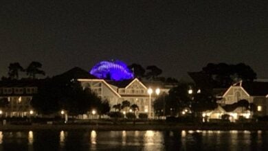 EPCOT at night with World Showcase buildings by the lagoon and Spaceship Earth glowing blue during Harmonious.