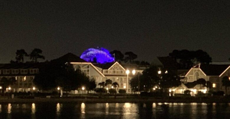 EPCOT at night with World Showcase buildings by the lagoon and Spaceship Earth glowing blue during Harmonious.