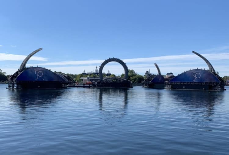 The iconic Harmonious arches rise over the World Showcase Lagoon at EPCOT, shimmering under a clear blue sky.