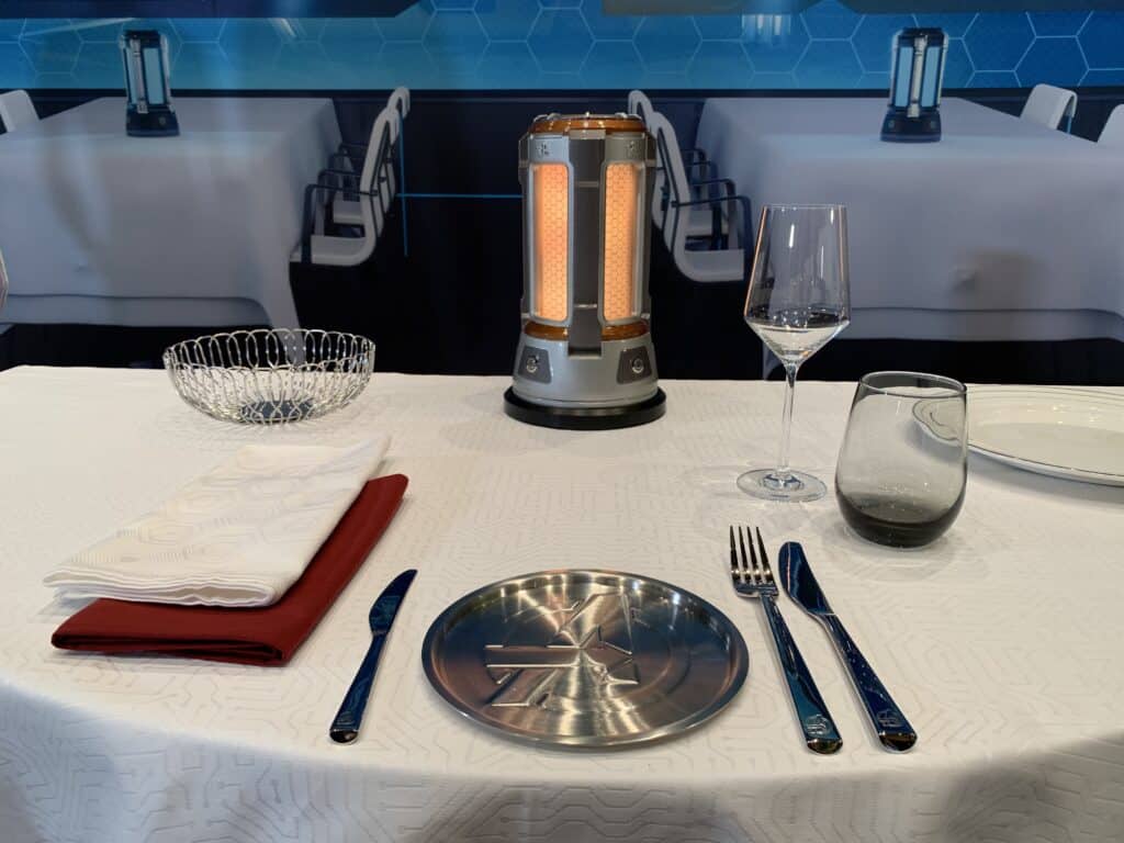 Elegant table setting on white linen with a futuristic lamp, echoing the magical dining aboard Disney Wish on Disney Cruise Line.