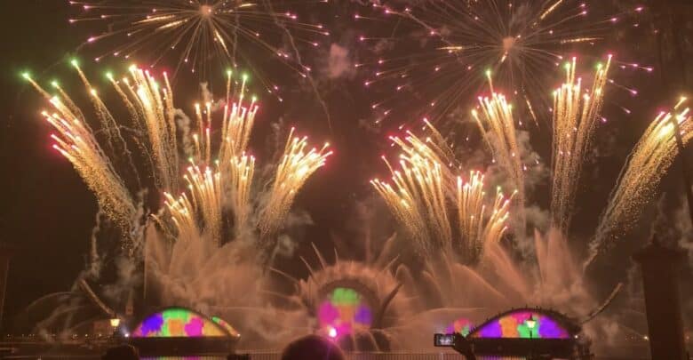 Fireworks and dazzling water fountains light up the night sky as guests watch in awe at a theme park nighttime spectacular.
