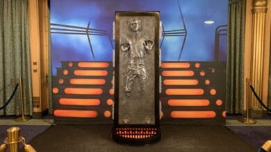 Han Solo frozen in carbonite greets guests with dramatic flair before Star Wars-themed red-lit steps and a futuristic backdrop.