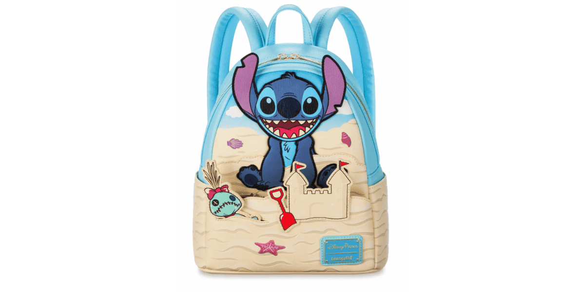 A light blue backpack featuring a playful Stitch from Disney's "Lilo & Stitch" sitting on a beige sandcastle design. The backpack has two padded straps, a zipper, and various beach-themed decorations, including a sand pail, shovel, and starfish.