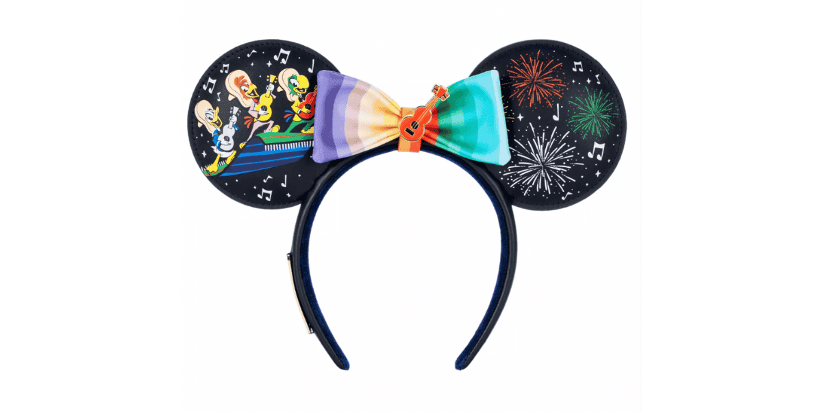 A headband featuring large round ears. The left ear depicts colorful animated characters playing instruments, while the right ear shows a fireworks display. A rainbow-colored bow with a small orange guitar at the center decorates the space between the ears.
