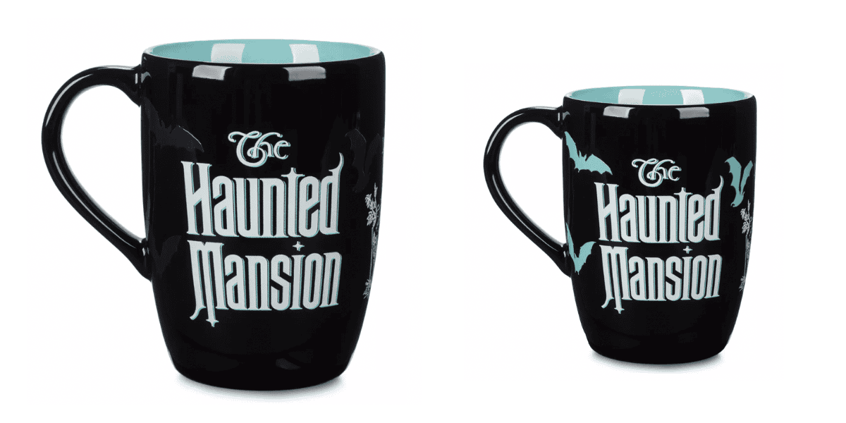 Two black ceramic mugs with a light blue interior. The larger mug features the words "The Haunted Mansion" in stylized white letters with bat and spider web designs. The smaller mug has a similar design with additional bat details, also featuring "The Haunted Mansion" text, part of the Haunted Mansion Kitchen Collection.