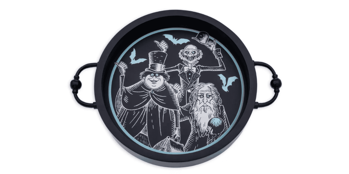A round black tray from the Haunted Mansion Kitchen Collection features a whimsical illustration of three spooky, ghostly characters in top hats with bats flying around them. The tray, which has two handles on opposite sides, enhances both its design and utility.