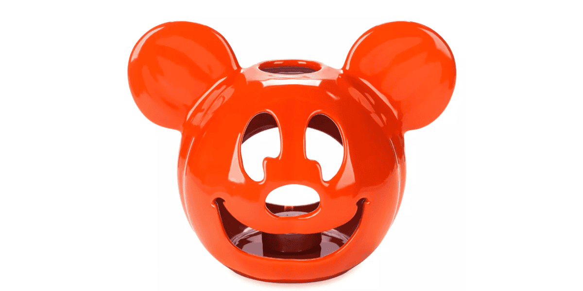 A bright orange ceramic candle holder shaped like the head of a cartoon mouse, with cutouts for the eyes, nose, and mouth. The design is playful and has two round ears protruding from the top.