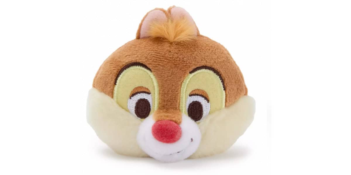 A plush toy of a chipmunk character with brown fur, a red nose, cream cheeks, and a tuft of orange hair on top, smiling with embroidered eyes and features.
