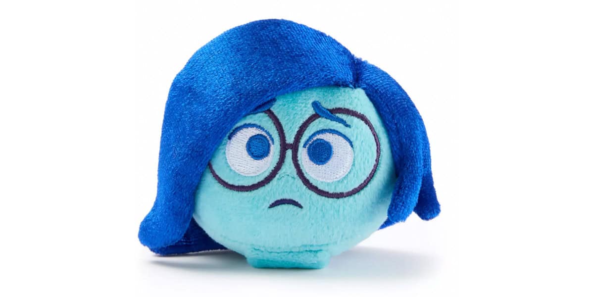 A plush toy with blue hair, large round glasses, and a sad facial expression, inspired by the character Sadness from the movie Inside Out, is shown against a white background.