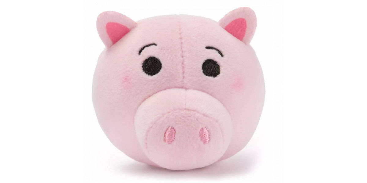 A round, plush pink pig toy with small ears, large nose, black embroidered eyes, and subtle blushing cheeks, against a white background.