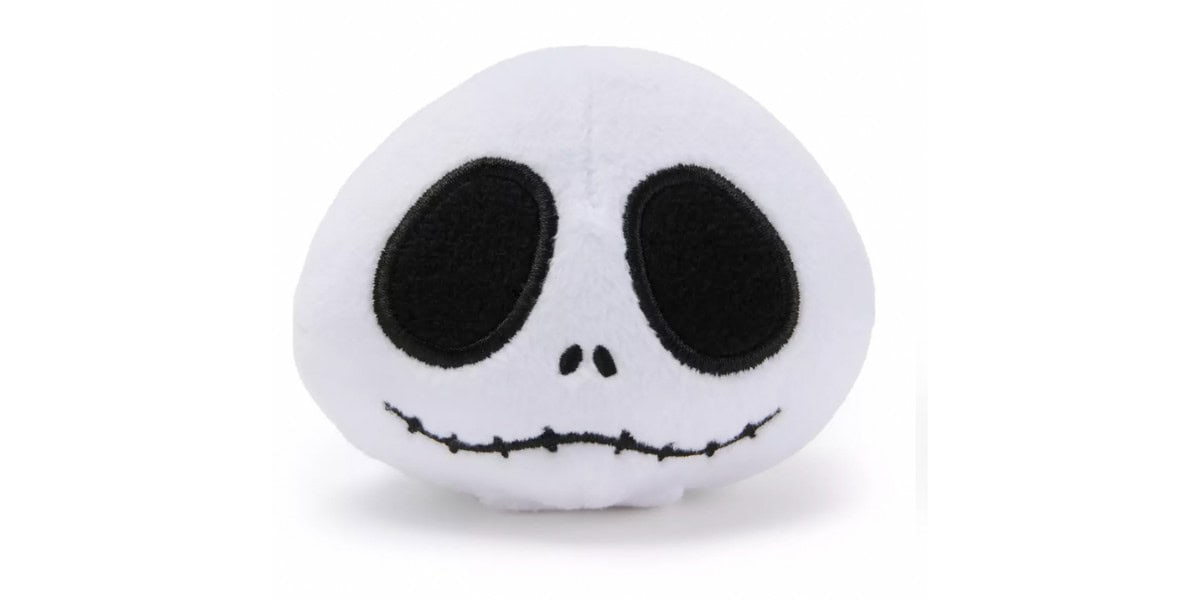 A plush toy shaped like a white skull with large black eye sockets and a stitched smile, resembling a cartoon or movie character, against a plain white background.
